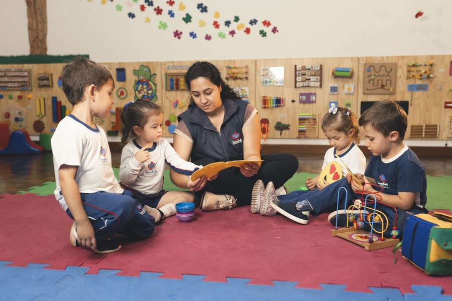 Professora lendo um livro para crianças da Educação Infantil sentadas no tapete da sala