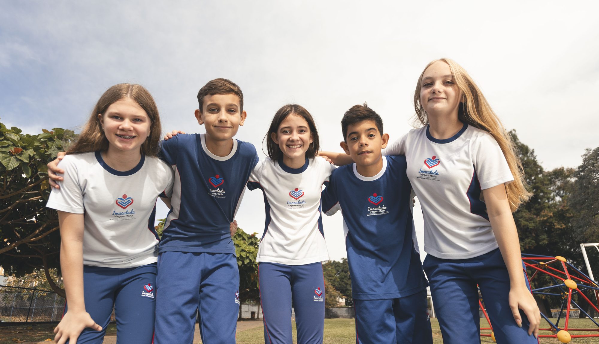 Cinco alunos do Colégio Imaculada Virgem Maria abraçados no pátio, de uniforme